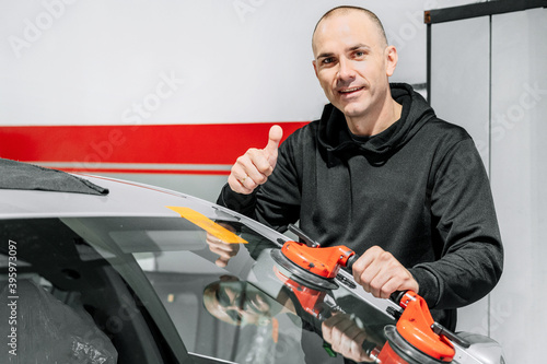 Automobile technician worker replacing windscreen or windshield of a car in auto service station garage. High quality photo