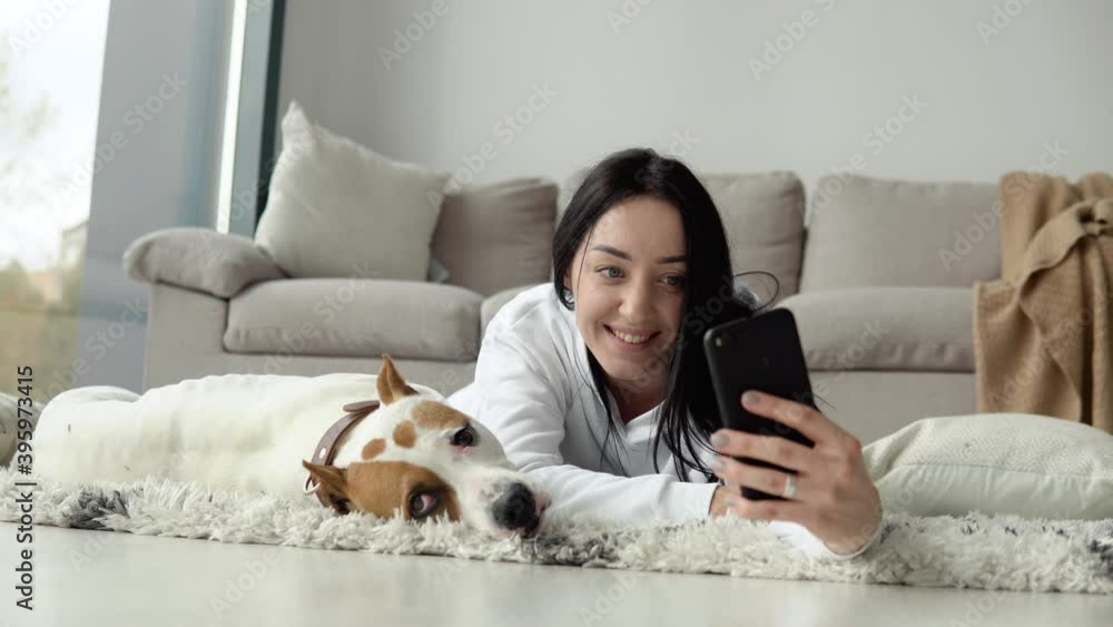 Young woman takes a selfie with her dog and use phone in a beautiful modern apartment