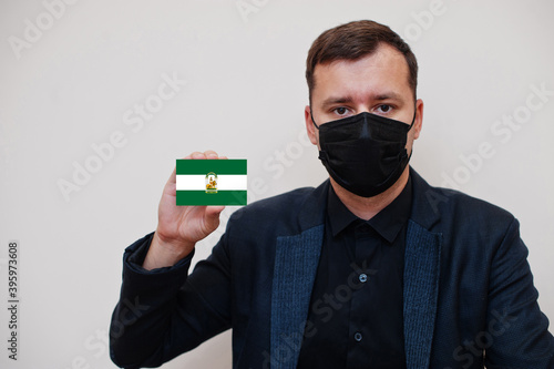 Spanish man wear black formal and protect face mask, hold Andalusia flag card isolated on white background. Spain autonomous communities coronavirus Covid concept.