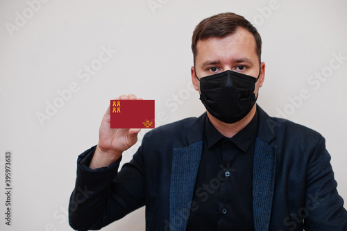 Spanish man wear black formal and protect face mask, hold Region of Murcia flag card isolated on white background. Spain autonomous communities coronavirus Covid concept.