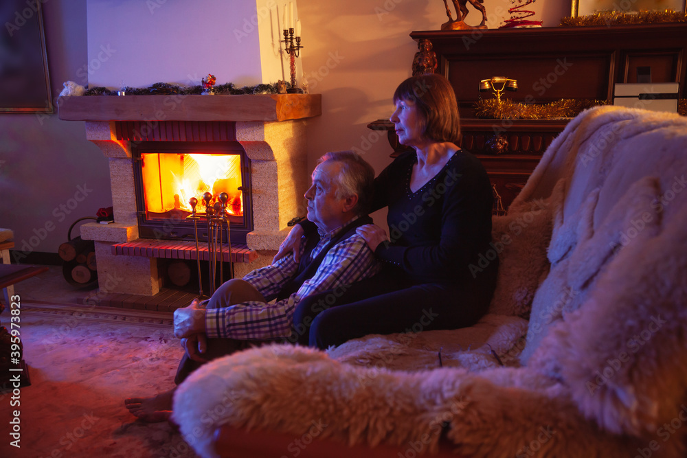 Elderly married couple sitting in front of fireplace in dark room