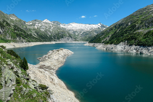 Dam in Austrian Alps. The artificial lake stretches over a vast territory, shining with navy blue color. The dam is surrounded by high mountains. In the back there is a glacier. Controlling the nature