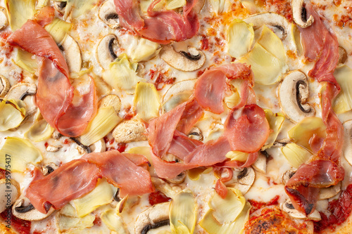 A top down view of a Mediterranean pizza, featuring toppings as prosciutto, artichoke and mushroom.