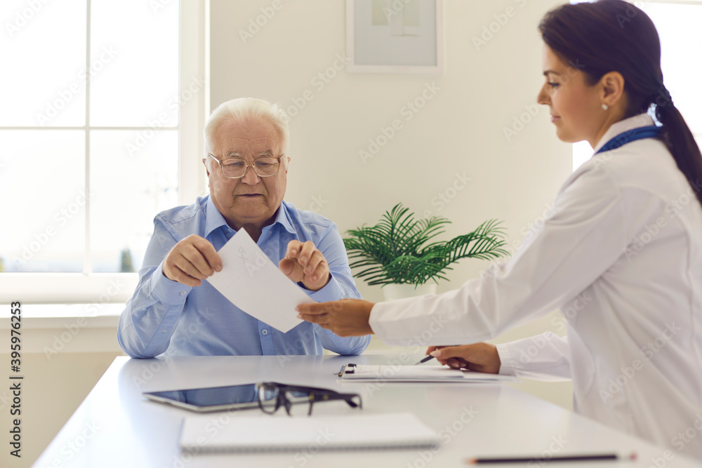 Obraz premium Smiling woman doctor giving paper prescription to elderly man patient in clinic