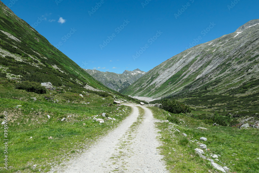 A gravelled road in high Alpine region of Maltal in Austria. The road is going slightly up. There is a huge glacier in the back. Clear and sunny day. Serenity and solitude