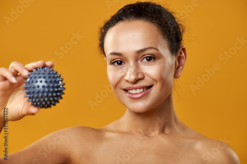 Beautiful african woman showing massage ball to camera isolated on yellow