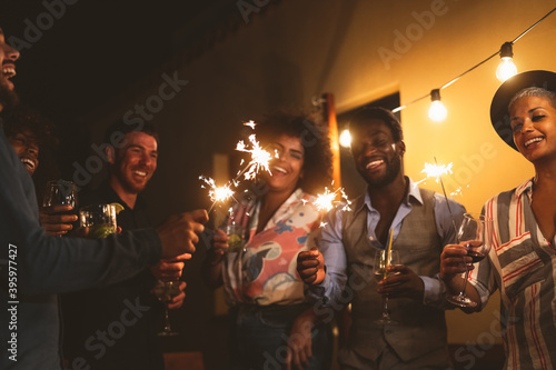 Happy young friends celebrating new year eve with sparklers fireworks and drinking cocktails on patio house party - Youth people lifestyle and holidays concept
