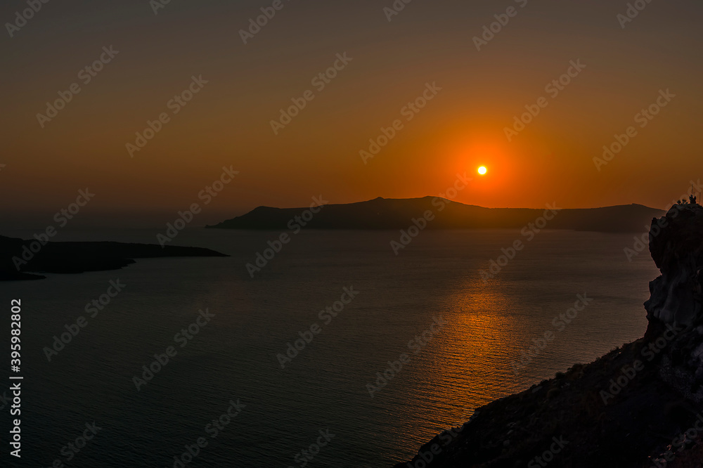 The sun sinks low in the sky viewed from Thira, Santorini at sunset in summertime