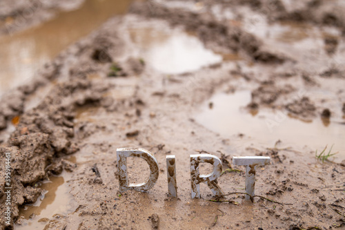 the word dirt composed of silver metal letters on wet clay surface photo