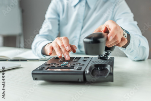 Cropped view of businesswoman with handset dialing number on landline telephone at table on blurred 