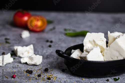 Feta traditional Greek cheese in a black tray with tomato on grey background
