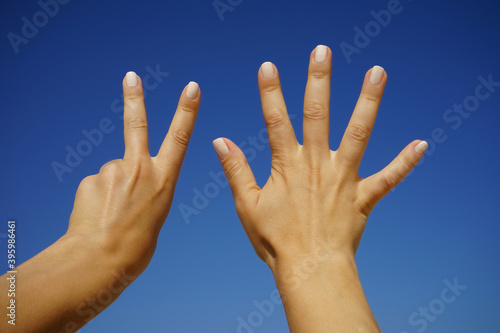 women's hands show the number seven against a cloudless blue sky