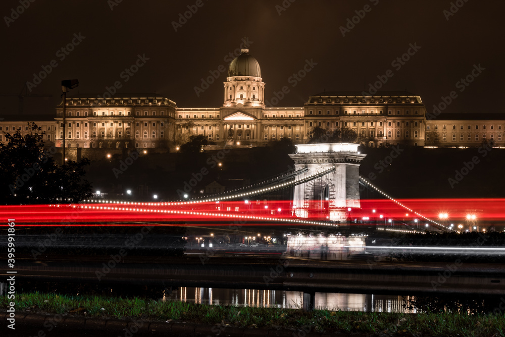 Floodlit Buda Castle in Budapest, Hungary during a cold night in November, with the Chain Bridge and the Danube river with car lights in the foreground
