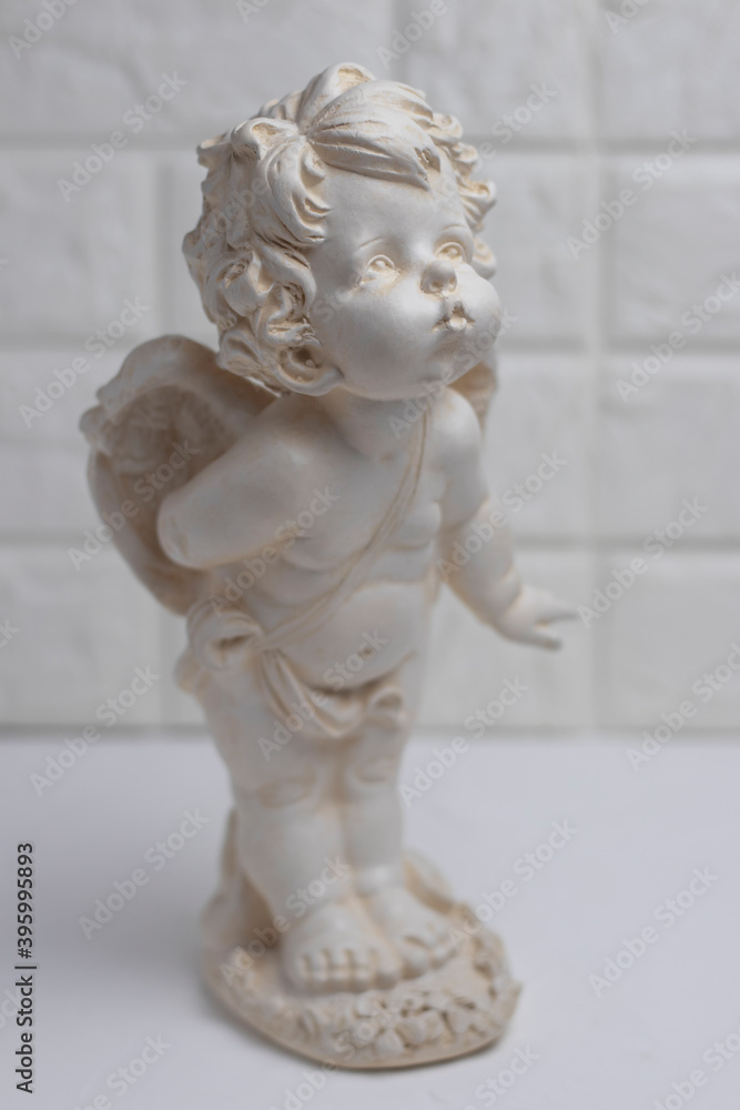 White plaster figurine of an angel on a brick wall background. Decorations in the interior.
