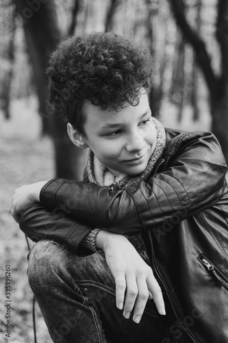 Curly brown-haired boy with a mohawk hairstyle in a leather jacket against the background of an autumn forest.
