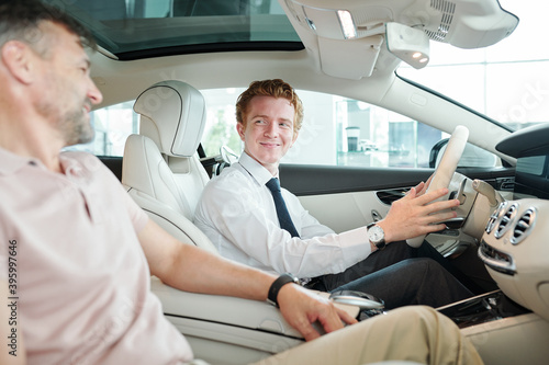Sales manager sitting in car and holding by steer during test drive with client