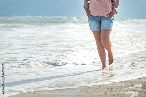 Barefoot middle age woman in summer casual outfit wolking on sea coast line © Денис Ржанов