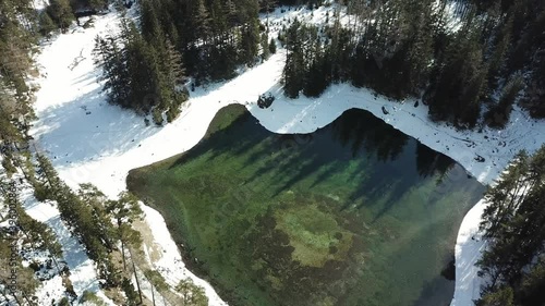 A drone shot of anAlpine valley in Austria. The valley has a Green Lake in the middle.  A headland in the middle of the lake. The algae give the lake distinctive color. Early spring in the mountains