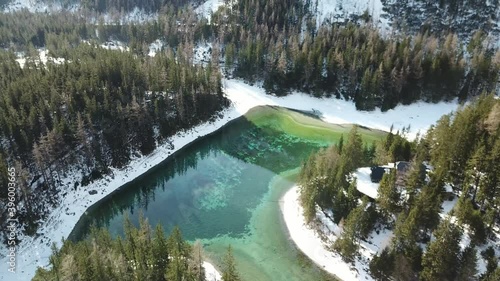 A drone shot of anAlpine valley in Austria. The valley has a Green Lake in the middle.  A headland in the middle of the lake. The algae give the lake distinctive color. Early spring in the mountains