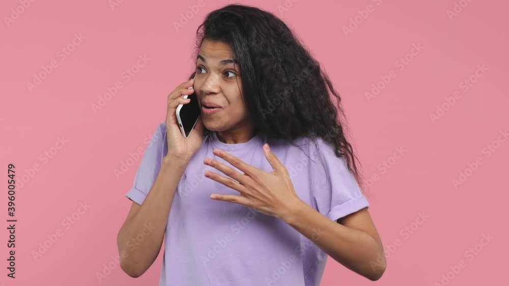 Surprised young african american woman 20s in violet t-shirt posing isolated on pink background in studio. People lifestyle concept. Talking on mobile cell phone put hand on chest doing winner gesture Surprised young african american woman 20s in violet t-shirt posing isolated on pink background in studio. People lifestyle concept. Talking on mobile cell phone put hand on chest doing winner gesture