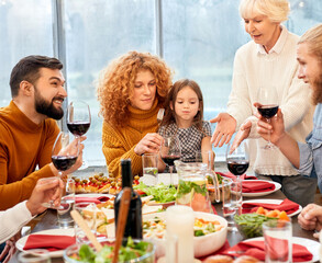 Family sitting behind served dinner table, holding wine glasses in hands