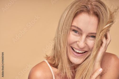 Happy pretty mature woman posing while touching hair by hands