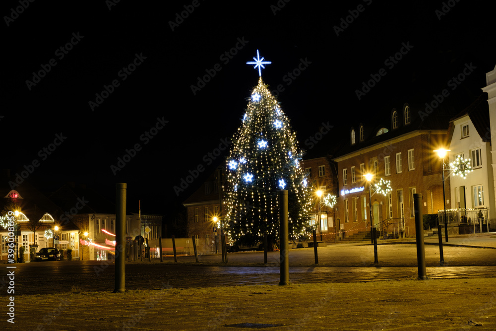 on a market place of a small town stands an illuminated Christmas tree