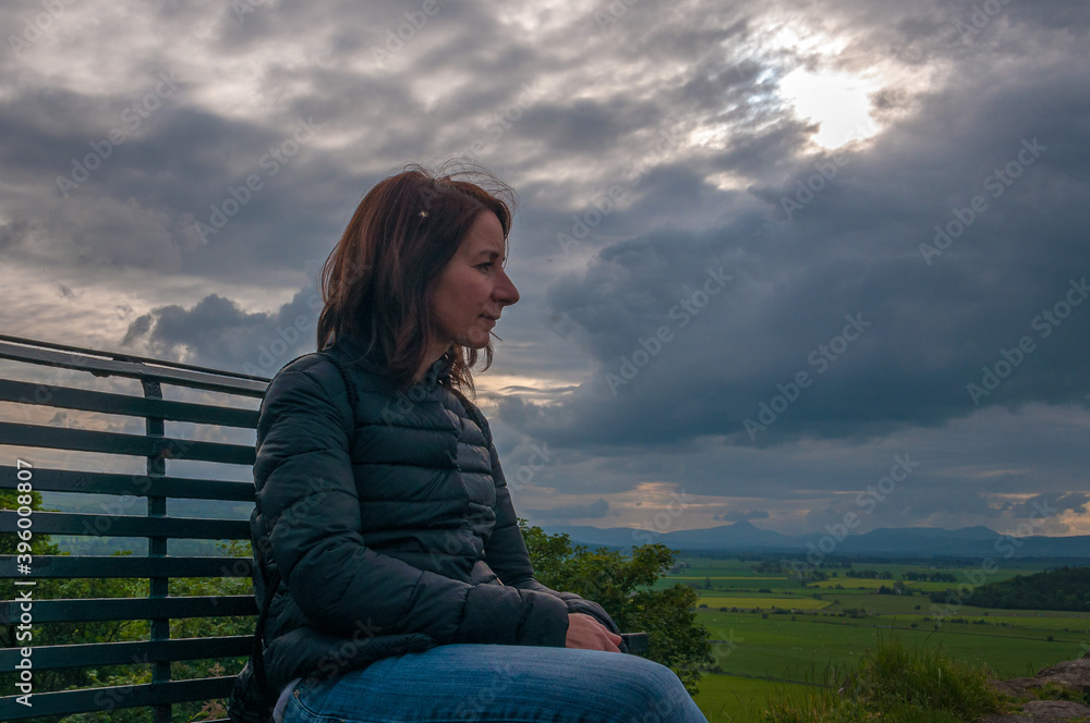 Girl sitting on a bench while contemplating thoughtfully the landscape in a cloudy day. Concept: relax in places with charm and mystery, travel to Scotland Girl sitting on a bench while contemplating thoughtfully the landscape in a cloudy day. Concept: relax in places with charm and mystery, travel to Scotland