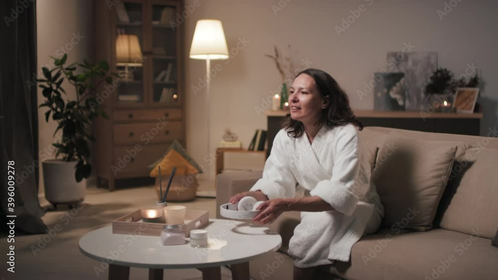 Medium shot of happy beautiful woman in white towel and bathrobe enjoying evening time sitting on sofa in headphones listening to music relaxing after hard day Medium shot of happy beautiful woman in white towel and bathrobe enjoying evening time sitting on sofa in headphones listening to music relaxing after hard day