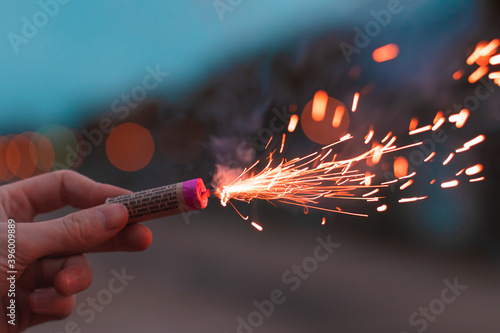 Young Man Lighting Up Firecracker in his Hand Outdoors in Evening. Guy Getting Ready for New Year Fun with Fireworks or Pyrotechnic Products - CloseUp Shot