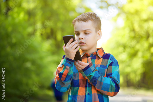 An emotional child is talking on a mobile phone in a Park on a Sunny summer day.