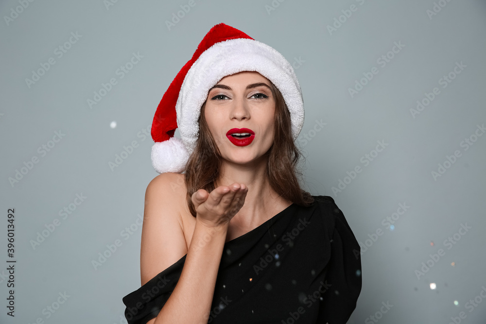 Beautiful woman in Santa hat blowing glitter on grey background. Christmas party Beautiful woman in Santa hat blowing glitter on grey background. Christmas party