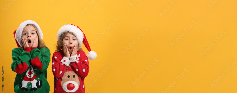 Fototapeta premium Kids in Christmas sweaters and Santa hats on yellow background, space for text