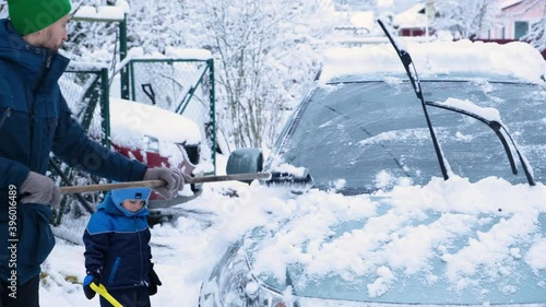 Father and son cleaning car from fresh snow after snowstorm. Maintaining an automobile in cold winter weather.