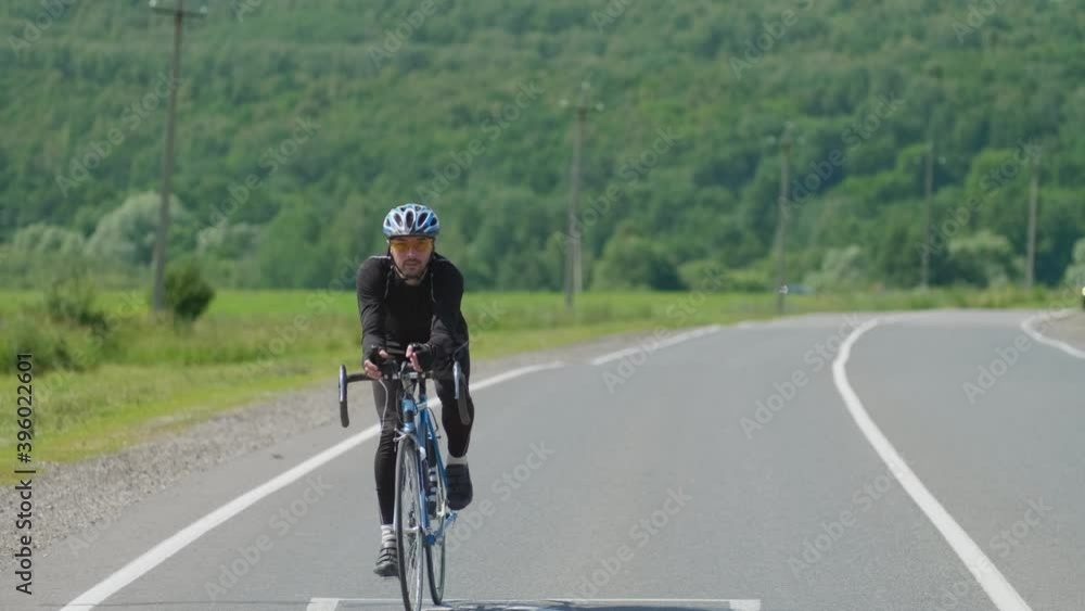 A professional cyclist in sports gear moves along an open paved road, beautiful nature on the horizon on a Sunny day. Selective focus A professional cyclist in sports gear moves along an open paved road, beautiful nature on the horizon on a Sunny day. Selective focus