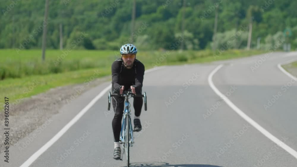 A professional cyclist in sports gear moves along an open paved road, beautiful nature on the horizon on a Sunny day. Selective focus A professional cyclist in sports gear moves along an open paved road, beautiful nature on the horizon on a Sunny day. Selective focus