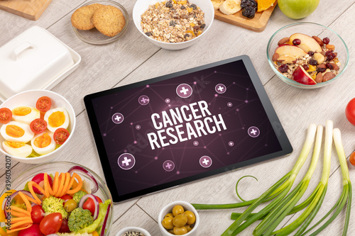 CANCER RESEARCH concept in tablet pc with healthy food around, top view