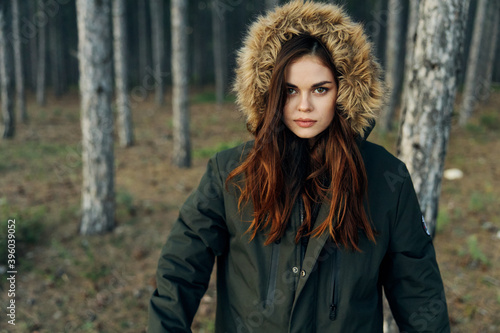 woman in a black jacket with a hood in nature looks ahead against the background of the forest © SHOTPRIME STUDIO