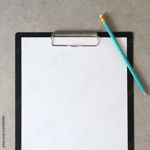Template of white paper with simple pencil on light grey concrete background in a black tablet with a clip. Concept of new idea, business plan and strategy. Stock photo with empty space for text