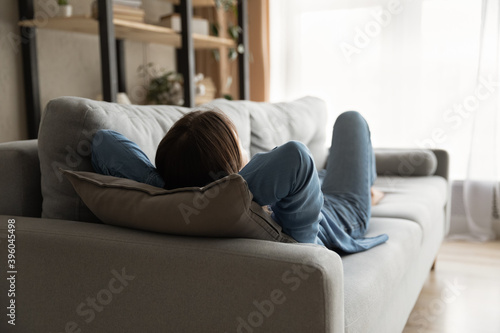 Back view of tired woman lying relaxing on comfortable sofa in living room take nap or daydream. Exhausted female rest on cozy couch at home, sleep relieve negative emotions. Stress free concept.