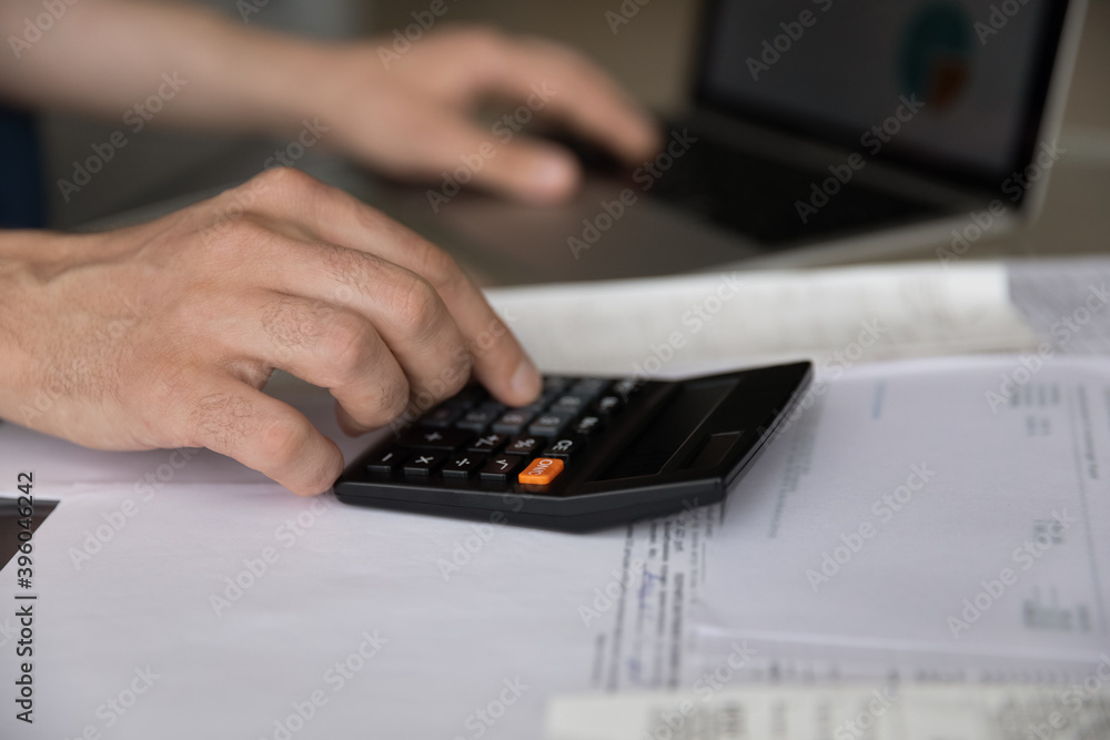 Crop close up of man count household expenses expenditures on calculator paying bills taxes on computer online. Male manage family budget or finances, make calculation. Saving, investment concept. Crop close up of man count household expenses expenditures on calculator paying bills taxes on computer online. Male manage family budget or finances, make calculation. Saving, investment concept.