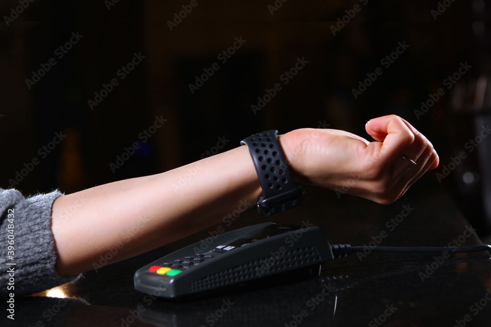 Fototapeta premium Payment using a wristwatch via a terminal in a restaurant or store. Female hand close-up with a watch when paying for a purchase. Copy space.