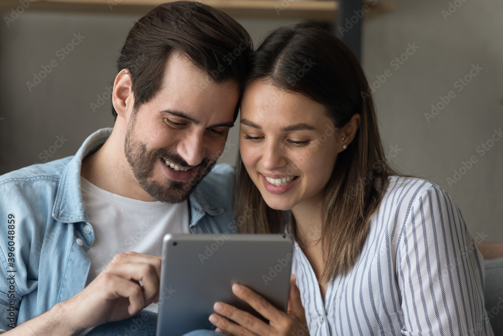 Close up of smiling young Caucasian couple look at tablet screen browse surf wireless internet on gadget. Happy man and woman use pad shopping online together on device. Technology concept. Close up of smiling young Caucasian couple look at tablet screen browse surf wireless internet on gadget. Happy man and woman use pad shopping online together on device. Technology concept.