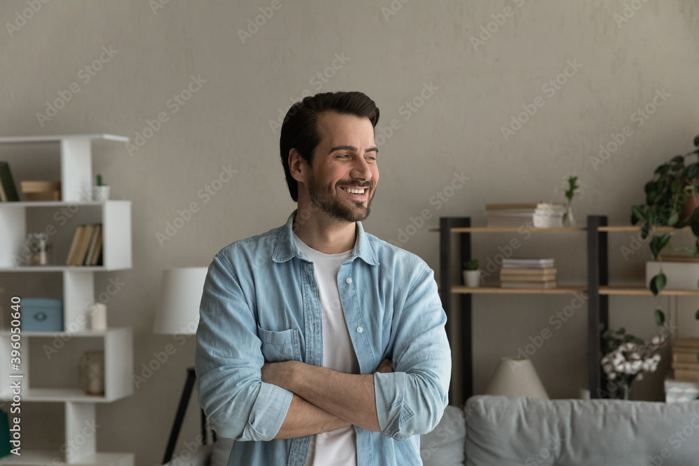 Fototapeta premium Happy young Caucasian man stand look in window distance thinking or planning future success. Smiling millennial male feel excited at home dreaming or visualizing opportunities. Vision concept.