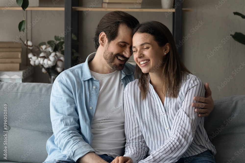 Happy millennial man and woman married spouses sit on sofa at home hugging cuddling. Smiling young Caucasian couple embrace enjoy tender intimate romantic moment together. Love, relations concept. Happy millennial man and woman married spouses sit on sofa at home hugging cuddling. Smiling young Caucasian couple embrace enjoy tender intimate romantic moment together. Love, relations concept.