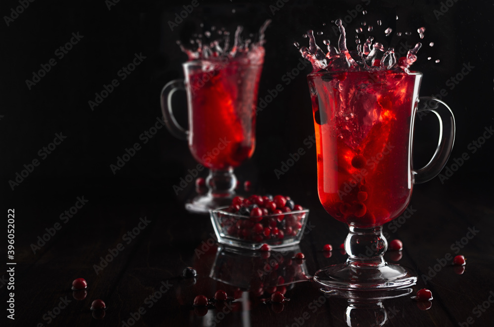Red berries tea with splash in two glasses wine glass with ripe berry in dark elegant black interior, copy space.