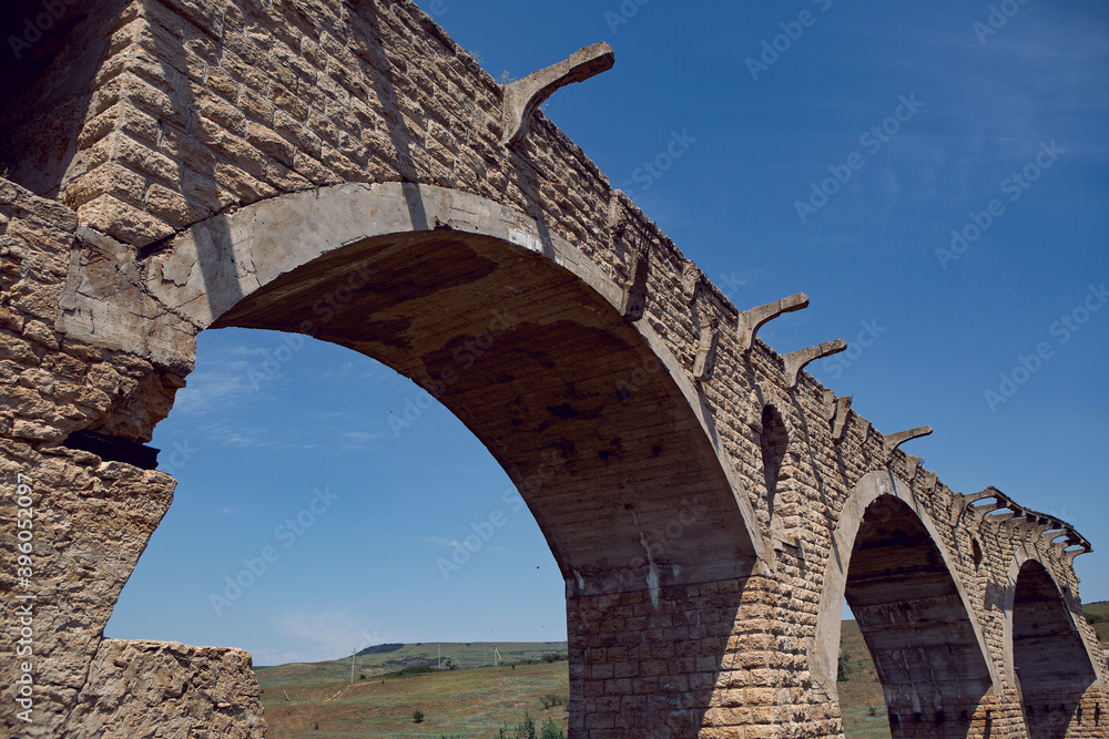 high ruined stone bridge stands in the summer in a field above the river in Russia