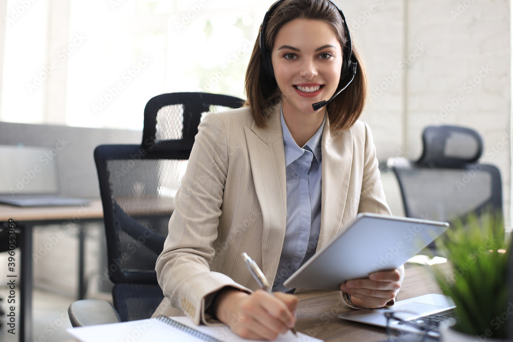 Cheerful female manager sitting at office desk and performing corporate tasks using wireless connection on digital gadgets. Cheerful female manager sitting at office desk and performing corporate tasks using wireless connection on digital gadgets.