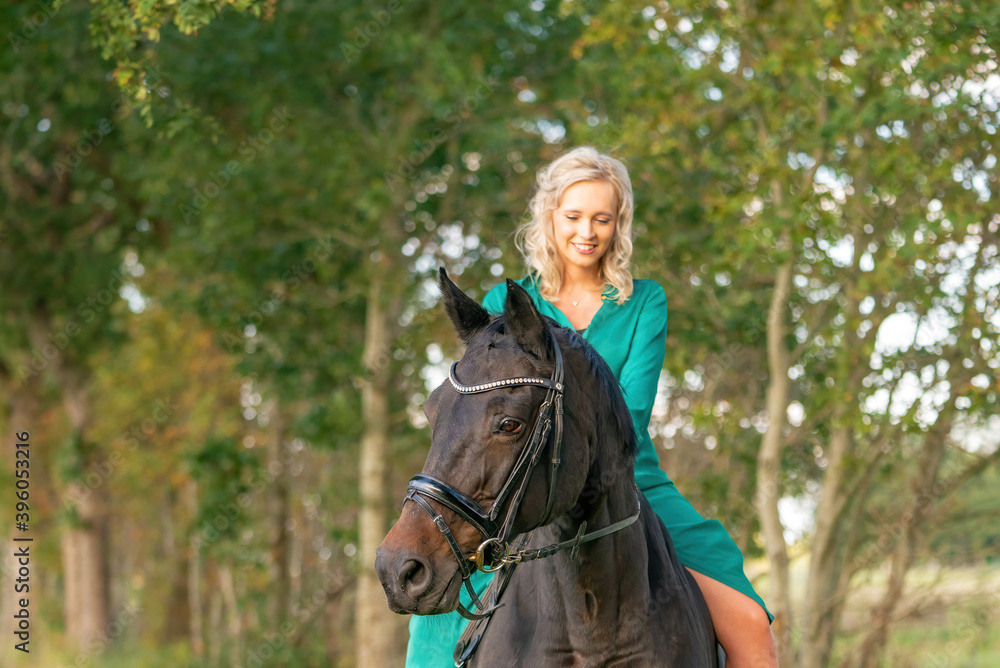 Portrait of a blonde girl in a vintage green dress with a big skirt posing with a brown horse. Selective focus
