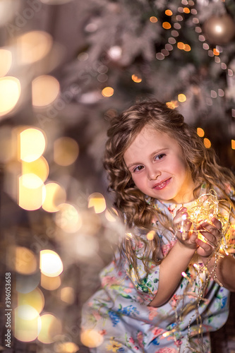 Portrait of a beautiful laughing girl with curly long hair on a background of blurred Christmas lights (bokeh) and a Christmas tree.